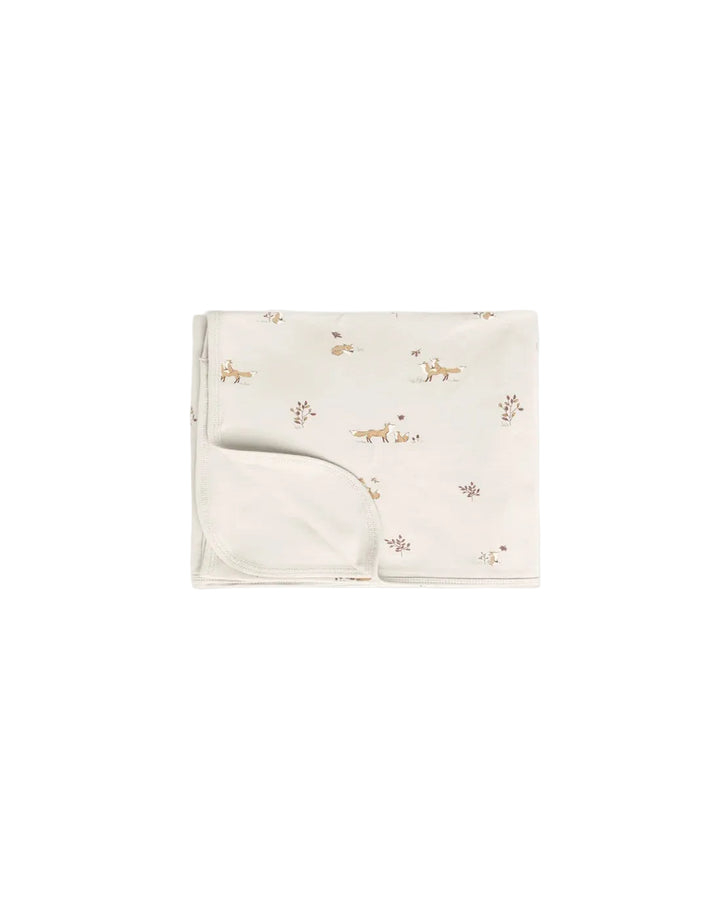 A folded baby blanket or swaddle in warm off-white fabric, printed with small tan and brown deer motifs and a soft matching folded corner, shown on a plain light background.