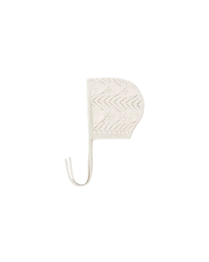 An off-white knit baby bonnet with a textured chevron pattern and a matching chin strap, shown against a solid white background.