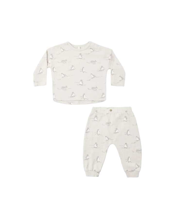 A two-piece baby clothing set featuring a long-sleeve top and matching pants in a warm off-white/cream color, both decorated with a delicate, all-over light gray bunny print. The set is laid flat on a clean, solid white background.