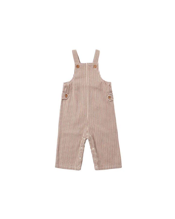 A baby romper in a pinkish-beige and white vertical stripe pattern, featuring adjustable shoulder straps with brown buttons and side pockets, shown flat on a light gray background.