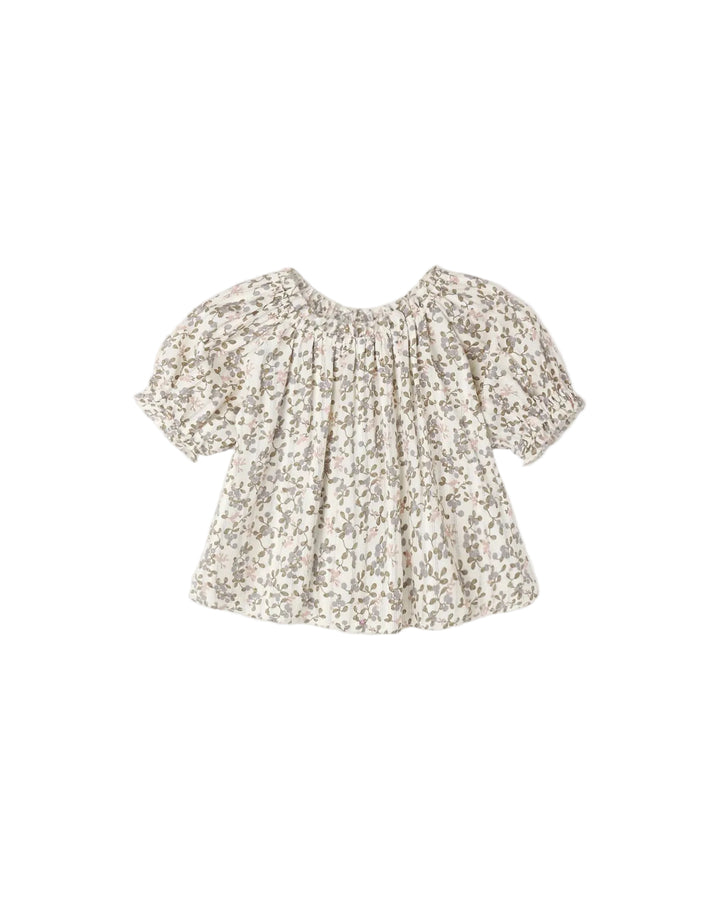 A short-sleeve baby top with a dense beige and brown floral print on a white background, featuring a smocked neckline and puffed sleeves, shown flat on a light gray background.