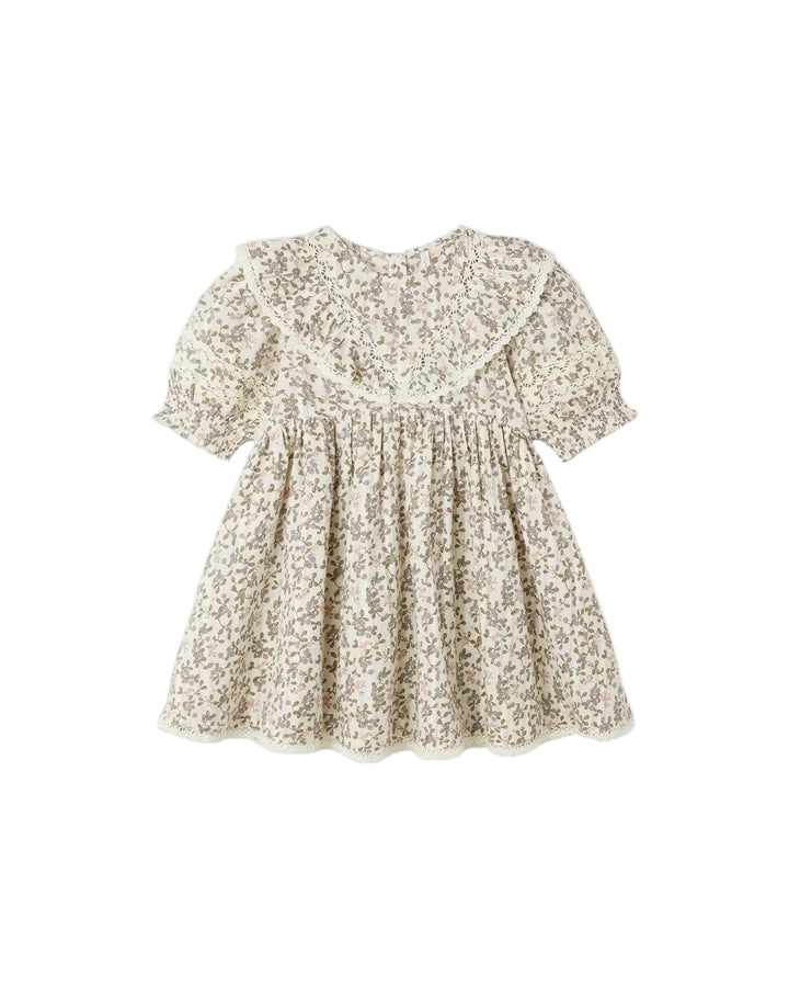 A short-sleeve baby dress with a beige and white floral print, featuring a ruffled collar and a gathered smocked bodice, shown against a plain light gray background.