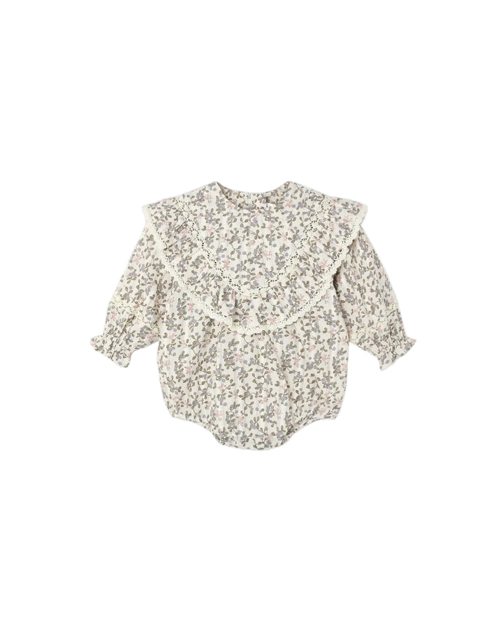 A baby long-sleeve romper with a large ruffled collar, featuring a dense small floral print in muted green, brown, and pink on an off-white base, shown against a plain light gray background.