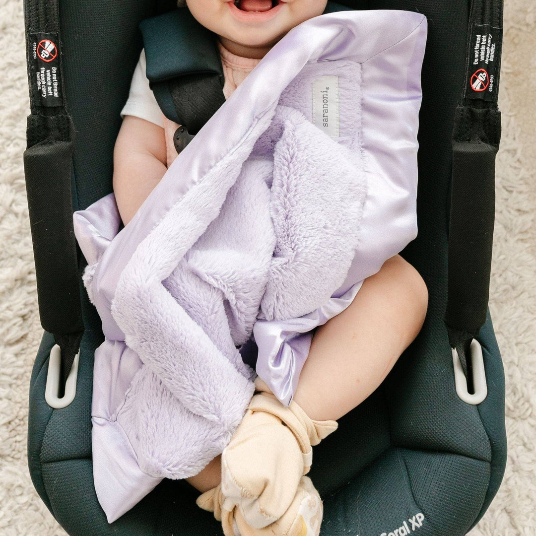 Baby in car seat with purple blanket and white socks.