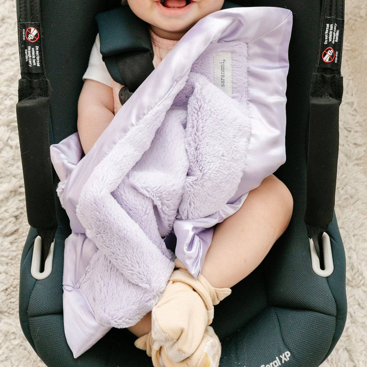 Baby in car seat with purple blanket and white socks.