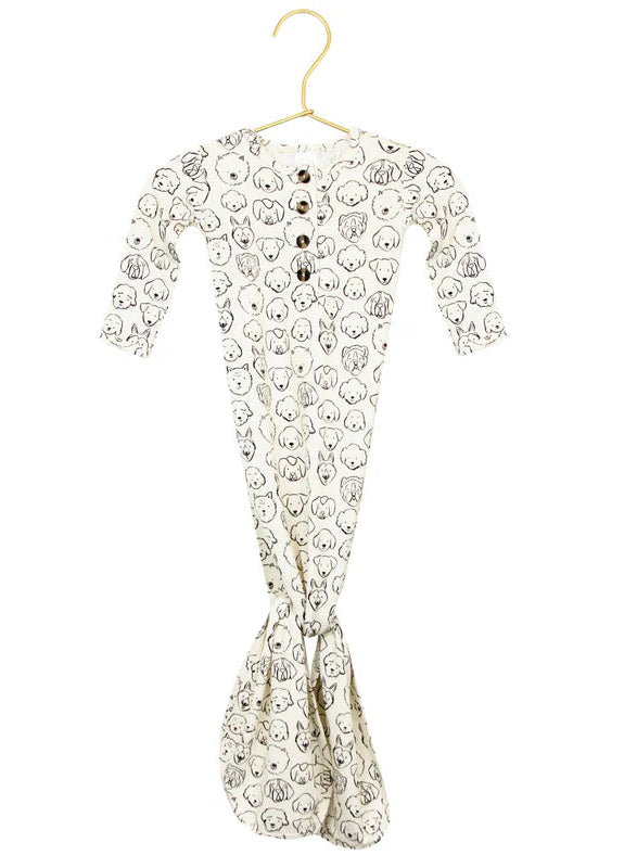 A knotted gown for babies with a pattern of dog faces, displayed on a hanger, with an inset showing a close-up of the dog face design.
