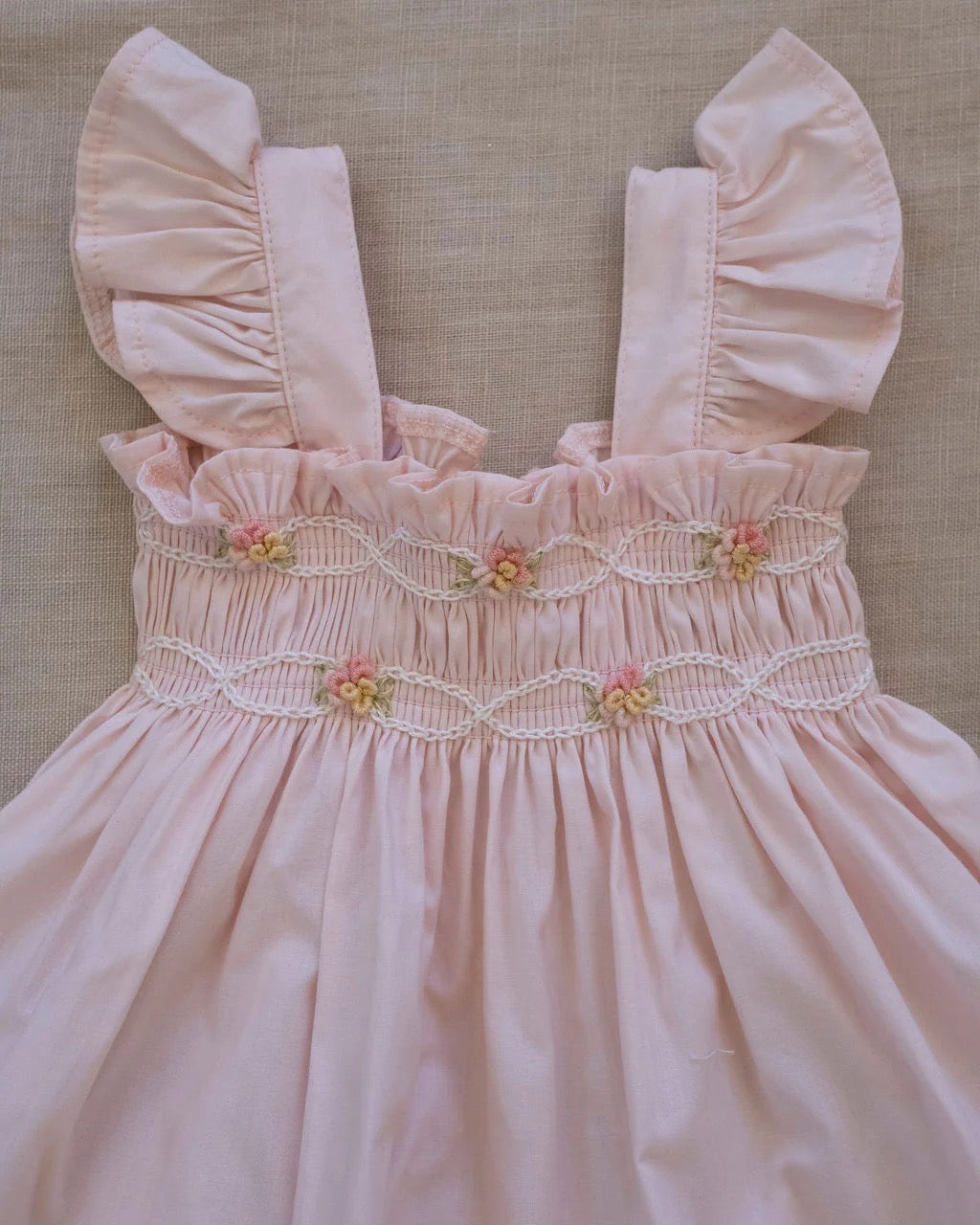 Hand-smocked flutter tunic with embroidered details and matching bloomers in soft pink on a white background.