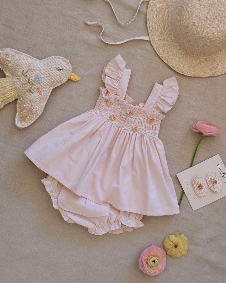 Hand-smocked flutter tunic with embroidered details and matching bloomers in soft pink on a white background.